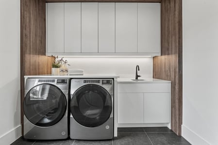 Modern laundry room with white cabinets and wood panel accents in River Oaks home by DesignLab