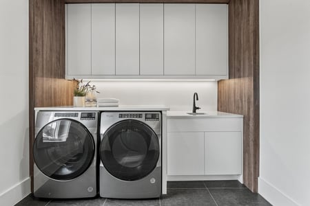 Modern laundry room with white cabinets and wood panel accents in River Oaks home by DesignLab