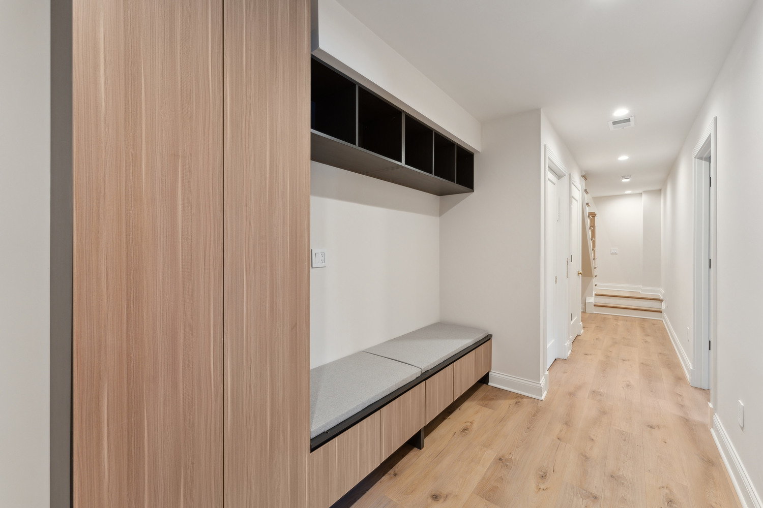 Sleek hallway mudroom with wood panel cabinetry and modern open shelving by DesignLab in Metro Washington custom home