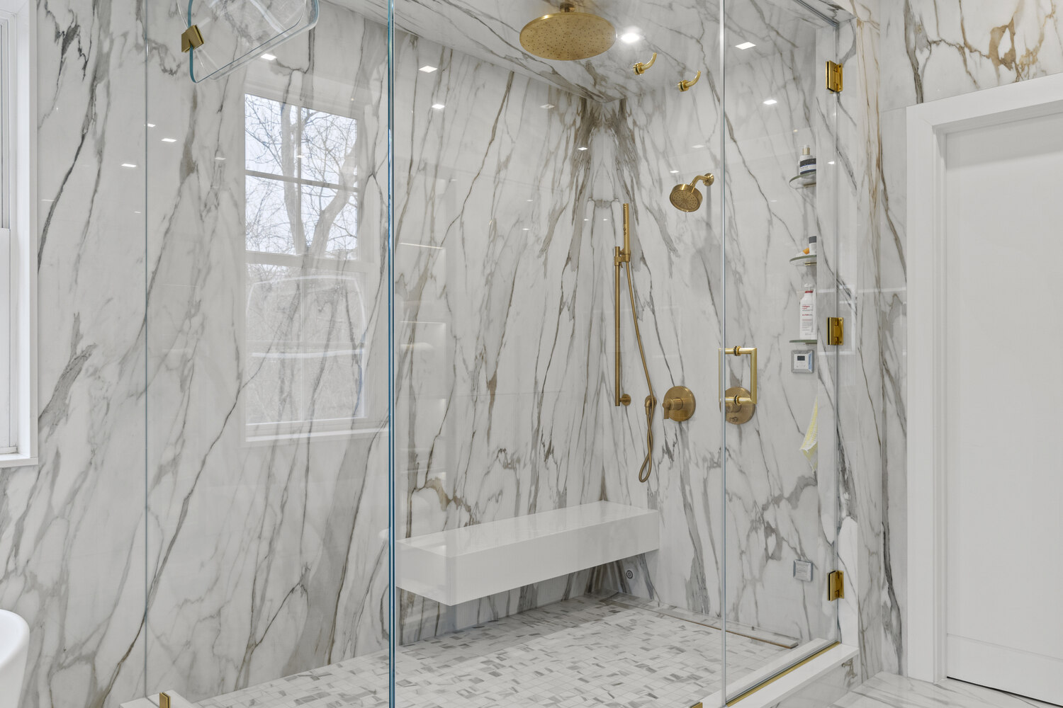 Marble walk-in shower with gold fixtures and bench seating in a Metro Washington custom home by DesignLab