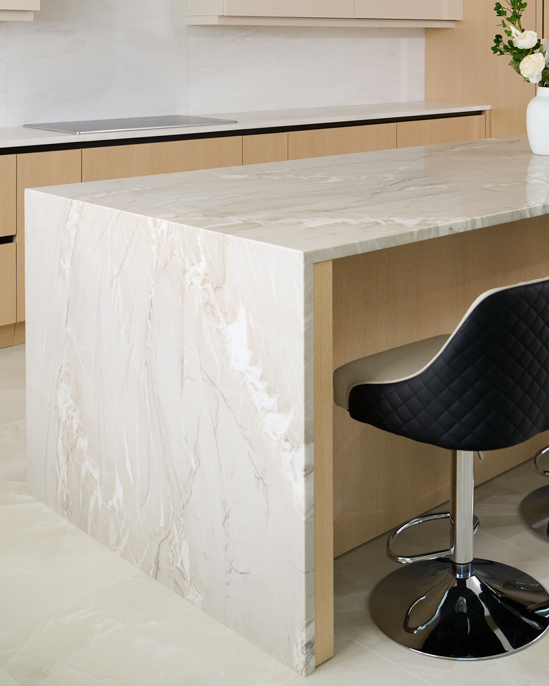 Waterfall-edge marble island with black bar stool in a modern kitchen by DesignLab in Potomac, MD